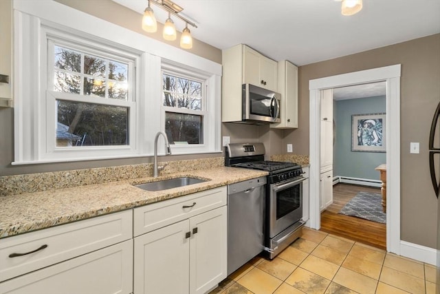 kitchen with appliances with stainless steel finishes, sink, white cabinets, light tile patterned floors, and light stone countertops