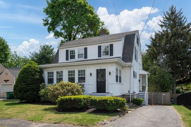 colonial inspired home featuring a chimney, roof with shingles, a gambrel roof, and asphalt driveway