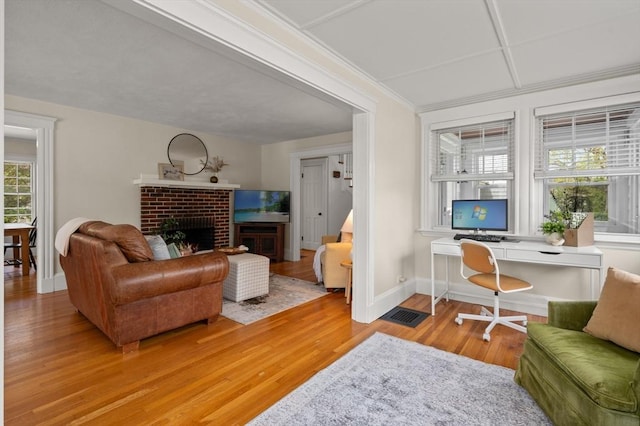 living area with light wood-type flooring, a brick fireplace, baseboards, and a desk