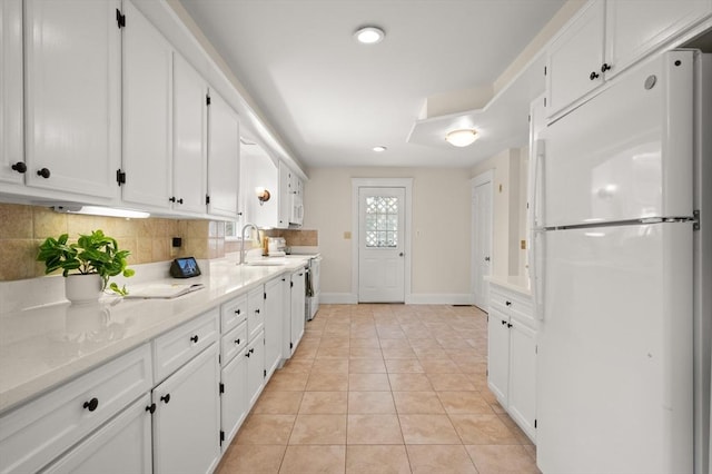 kitchen featuring freestanding refrigerator, white cabinets, a sink, baseboards, and tasteful backsplash