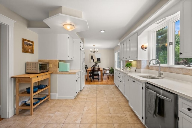 kitchen featuring dishwasher, a sink, light countertops, a chandelier, and decorative backsplash