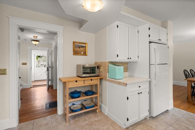 kitchen with freestanding refrigerator, light countertops, white cabinetry, and baseboards