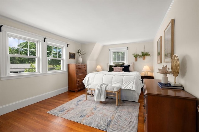 bedroom with multiple windows, wood finished floors, and baseboards