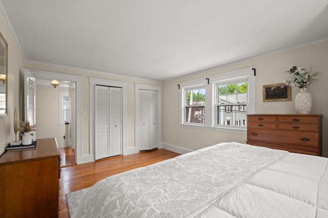 bedroom with multiple closets, wood finished floors, baseboards, and crown molding