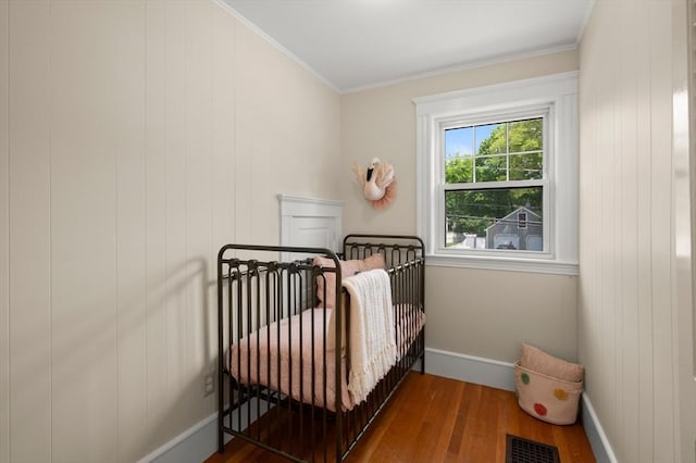 bedroom with wood finished floors, a nursery area, baseboards, and crown molding