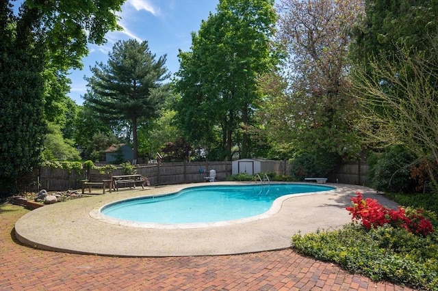 view of swimming pool featuring a storage unit, a fenced backyard, an outbuilding, and a patio