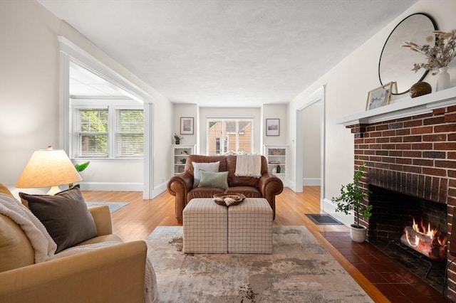 living room with a brick fireplace, wood finished floors, baseboards, and plenty of natural light