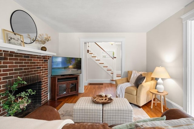 living room with stairs, wood finished floors, baseboards, and a fireplace