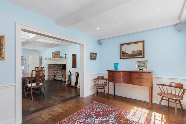 living area with a fireplace, beam ceiling, and dark wood-type flooring