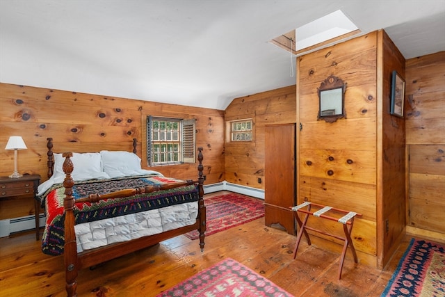 bedroom featuring vaulted ceiling with skylight, wooden walls, a baseboard heating unit, and hardwood / wood-style flooring