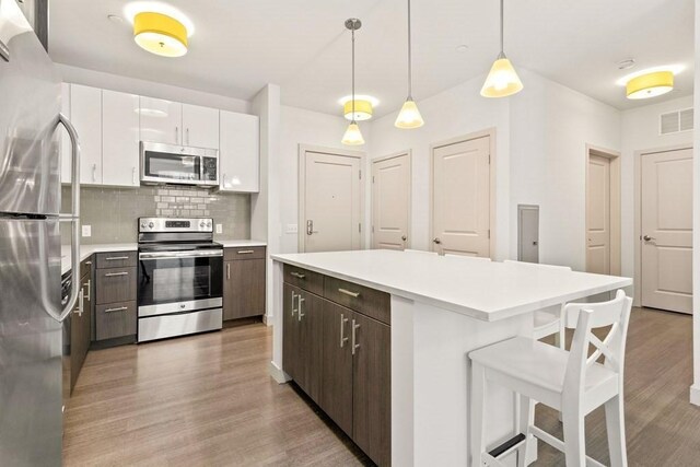 kitchen featuring light wood-style floors, appliances with stainless steel finishes, a breakfast bar area, and light countertops