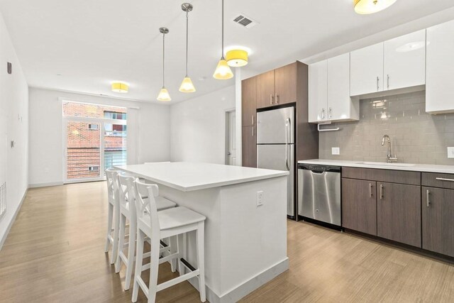 kitchen featuring visible vents, dishwasher, a sink, freestanding refrigerator, and light wood-style floors