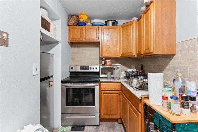 59 Harvard St, Everett, MA 02149 - kitchen featuring appliances with stainless steel finishes, light countertops, decorative backsplash, and light wood-style flooring