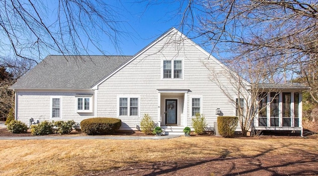 new england style home featuring a shingled roof, a front yard, and a sunroom