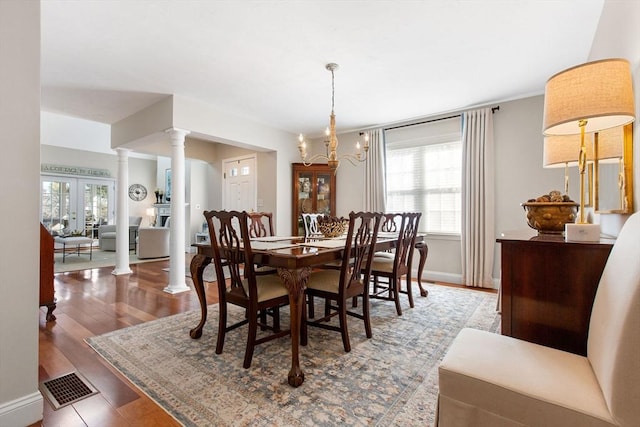 dining area featuring visible vents, baseboards, wood finished floors, a notable chandelier, and ornate columns