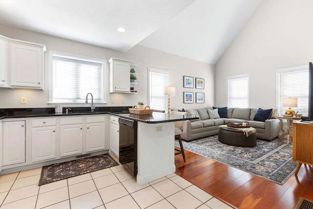 kitchen featuring a peninsula, dishwasher, open floor plan, and white cabinets