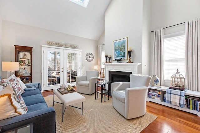 living area with french doors, a skylight, wood finished floors, a glass covered fireplace, and high vaulted ceiling