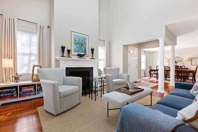 living area with hardwood / wood-style floors, a fireplace, decorative columns, baseboards, and a towering ceiling