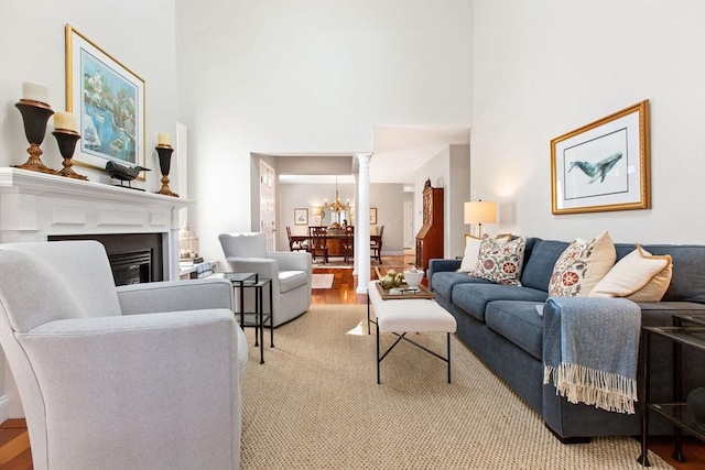 living room featuring decorative columns, an inviting chandelier, a glass covered fireplace, and light wood finished floors