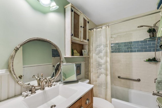 full bath with toilet, shower / tub combo with curtain, wainscoting, and vanity