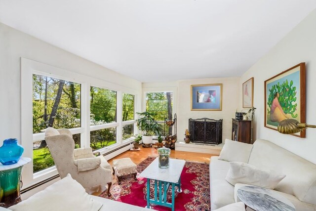 living room with a baseboard heating unit, plenty of natural light, and a fireplace with raised hearth