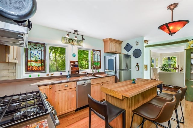 kitchen featuring stainless steel appliances, a sink, light wood-style floors, butcher block counters, and a breakfast bar area