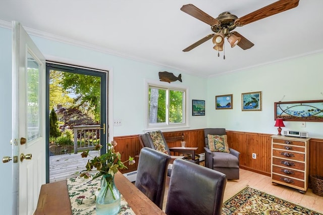 living area with healthy amount of natural light, a wainscoted wall, light wood-style flooring, ornamental molding, and a ceiling fan