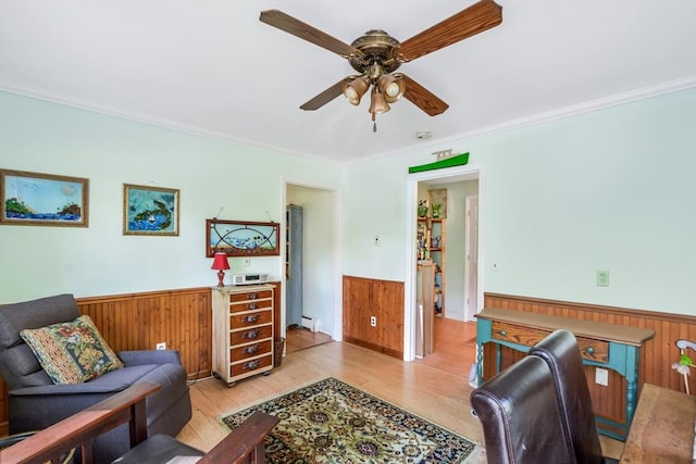 living area featuring a wainscoted wall, wood walls, ceiling fan, crown molding, and wood finished floors
