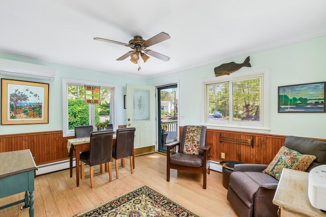 living area with baseboard heating, light wood-style flooring, a wall mounted air conditioner, wainscoting, and a ceiling fan