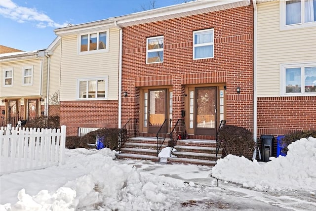 view of property with entry steps, brick siding, and fence