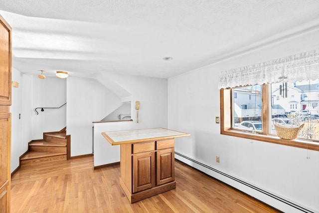 kitchen featuring tile countertops, a baseboard radiator, a kitchen island, baseboards, and light wood finished floors