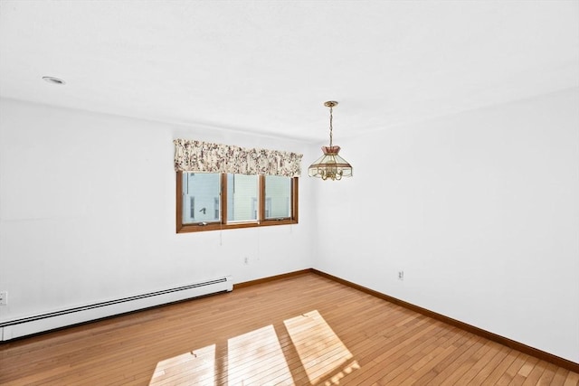 spare room with a baseboard heating unit, wood finished floors, and baseboards