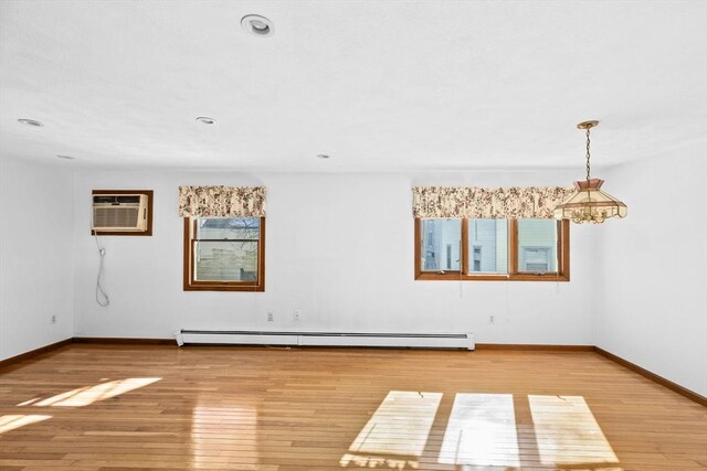 unfurnished room featuring a wall unit AC, a baseboard radiator, a wealth of natural light, light wood-type flooring, and baseboards