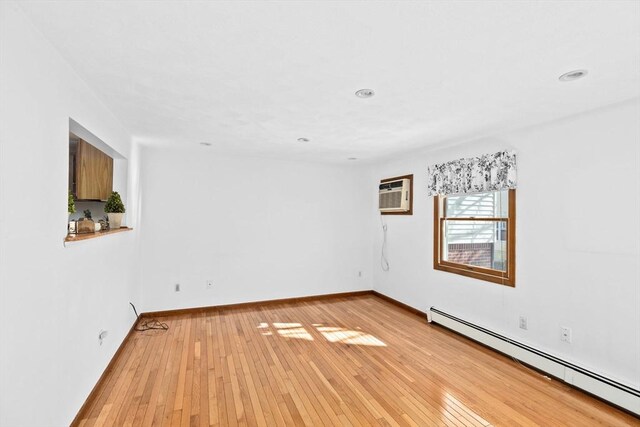 spare room featuring an AC wall unit, light wood finished floors, baseboard heating, and baseboards