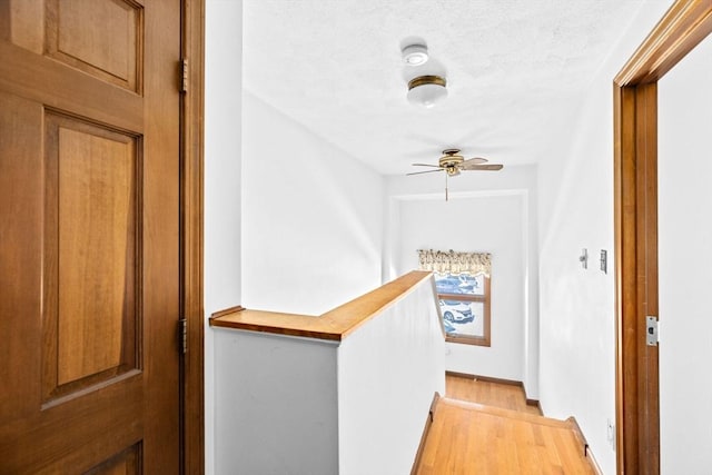 corridor featuring a textured ceiling, light wood finished floors, and an upstairs landing