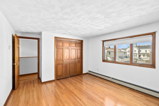 unfurnished bedroom featuring baseboards, light wood-style flooring, baseboard heating, a textured ceiling, and a closet