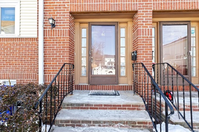 snow covered property entrance featuring brick siding