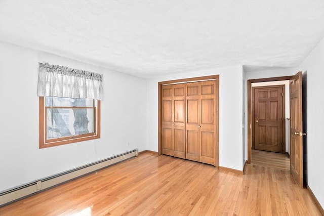 unfurnished bedroom with light wood-type flooring, baseboards, baseboard heating, and a closet