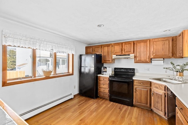 kitchen with light countertops, baseboard heating, a sink, under cabinet range hood, and black appliances