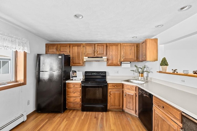 kitchen with brown cabinets, light countertops, baseboard heating, under cabinet range hood, and black appliances