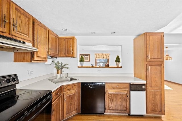 kitchen with under cabinet range hood, a sink, light countertops, brown cabinets, and black appliances