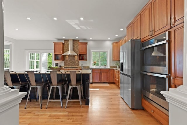 45 Anselm Way, Sudbury, MA 01776 - kitchen with stainless steel appliances, wall chimney exhaust hood, light wood-style floors, a breakfast bar area, and a sink