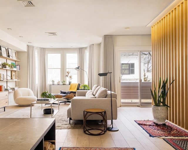 living area with light wood-style flooring, visible vents, and a healthy amount of sunlight