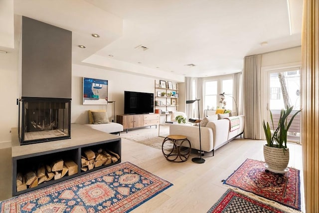 living room featuring recessed lighting, a multi sided fireplace, visible vents, and light wood finished floors