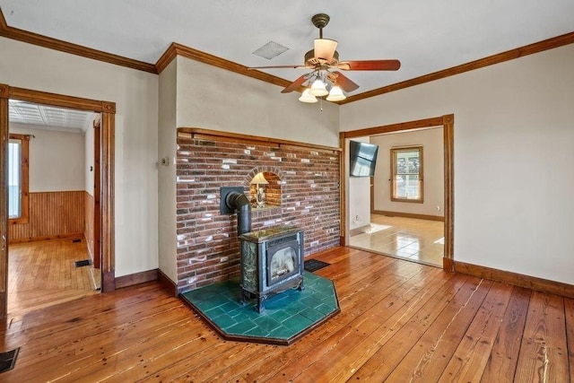 unfurnished living room featuring a wood stove, crown molding, light hardwood / wood-style flooring, and ceiling fan