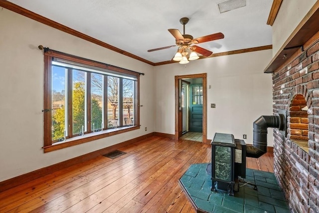 living room with hardwood / wood-style floors, ceiling fan, a wood stove, and ornamental molding