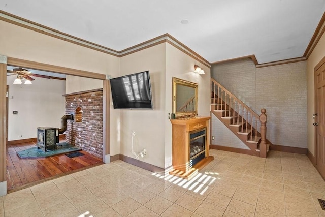 living room featuring a wood stove, crown molding, ceiling fan, light tile patterned floors, and brick wall