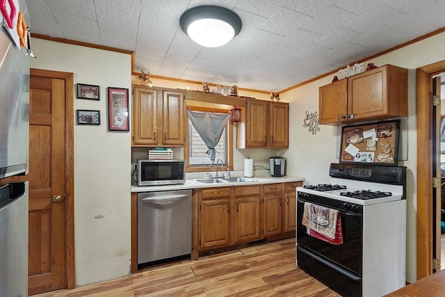 kitchen featuring light countertops, brown cabinets, appliances with stainless steel finishes, light wood-style floors, and a sink