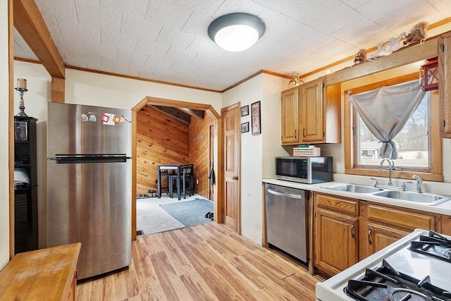 kitchen featuring light wood-style flooring, a sink, stainless steel appliances, wooden walls, and light countertops