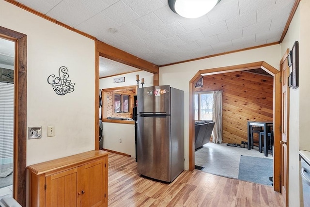 kitchen with light wood-style flooring, freestanding refrigerator, wood walls, and ornamental molding